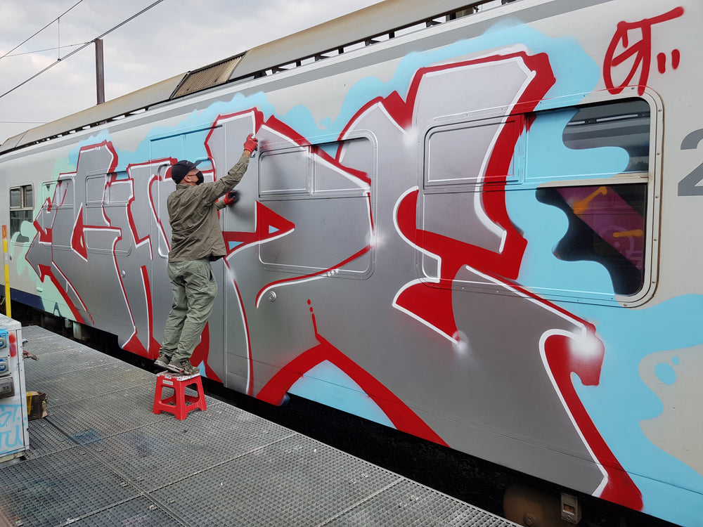 Writer painting a silver and red piece on a train at a platform