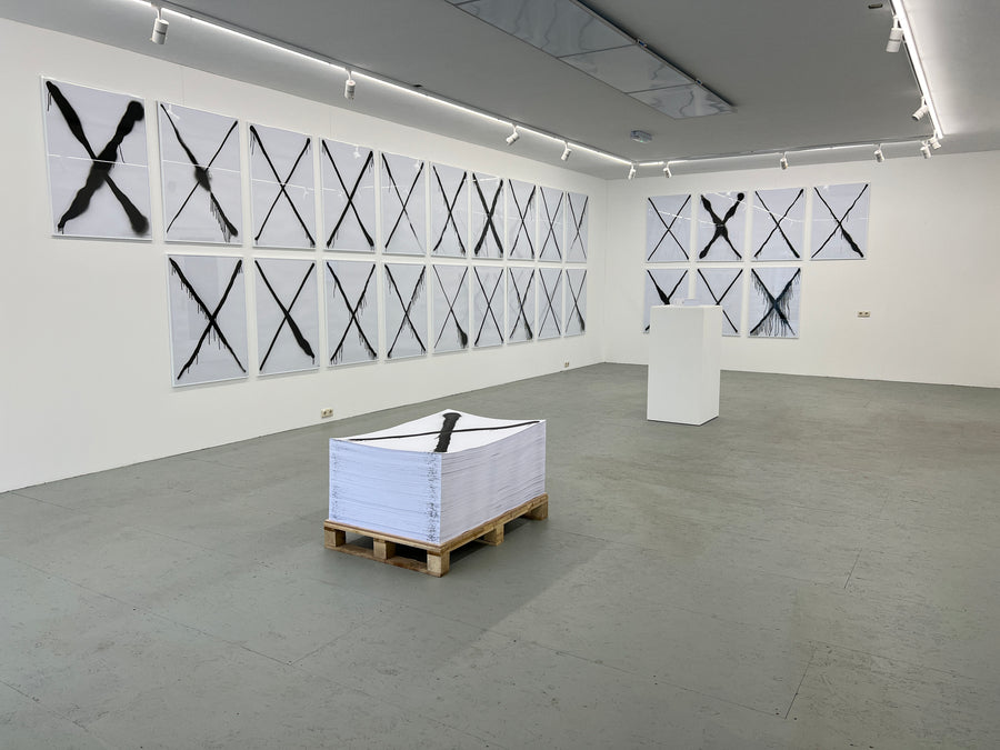 MONOMANIA exhibition: spray-painted crosses on the gallery walls and a stack of prints on a pallet