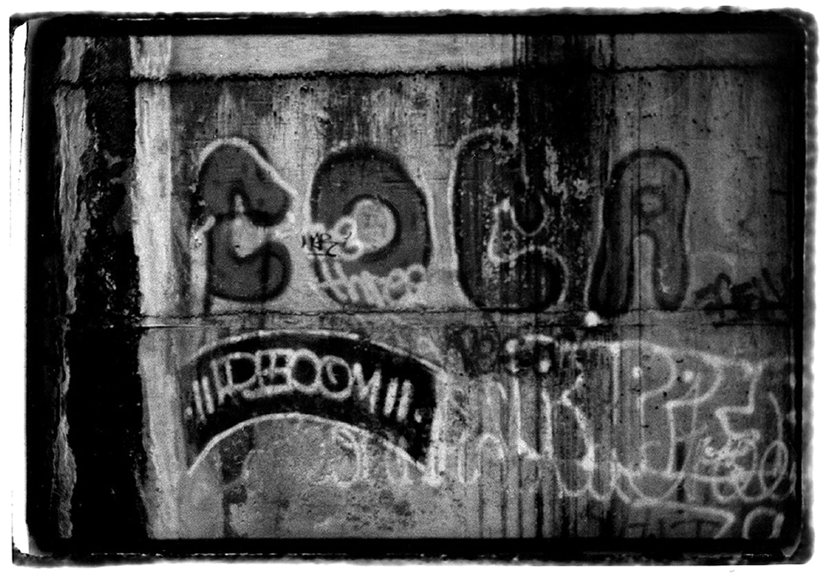 Black-and-white photograph of a Coca 82 piece on a wall, 1985